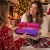 Kobieta wręcza drugiej kobiecie pudełko kul do kąpieli z kokardą przy choince