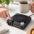 Palec dotyka panelu podgrzewacza do kubka, druga dłoń trzyma kubek kawy